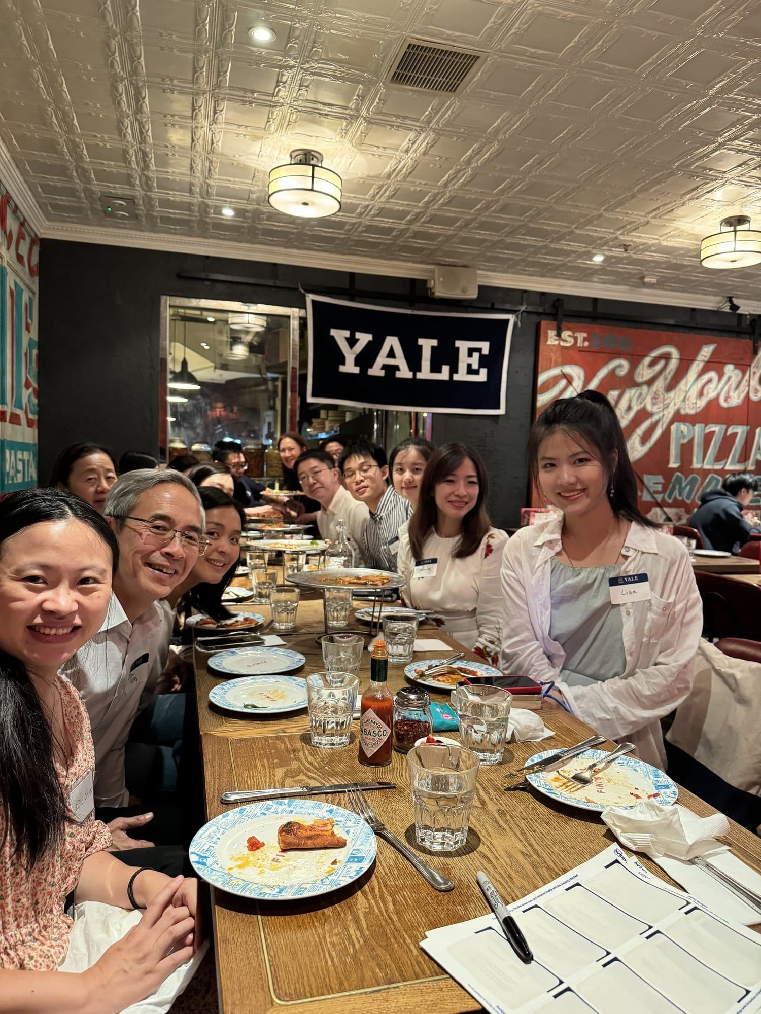 Yale alumni at a long table under a Yale banner at a New Haven pizza lunch in Hong Kong