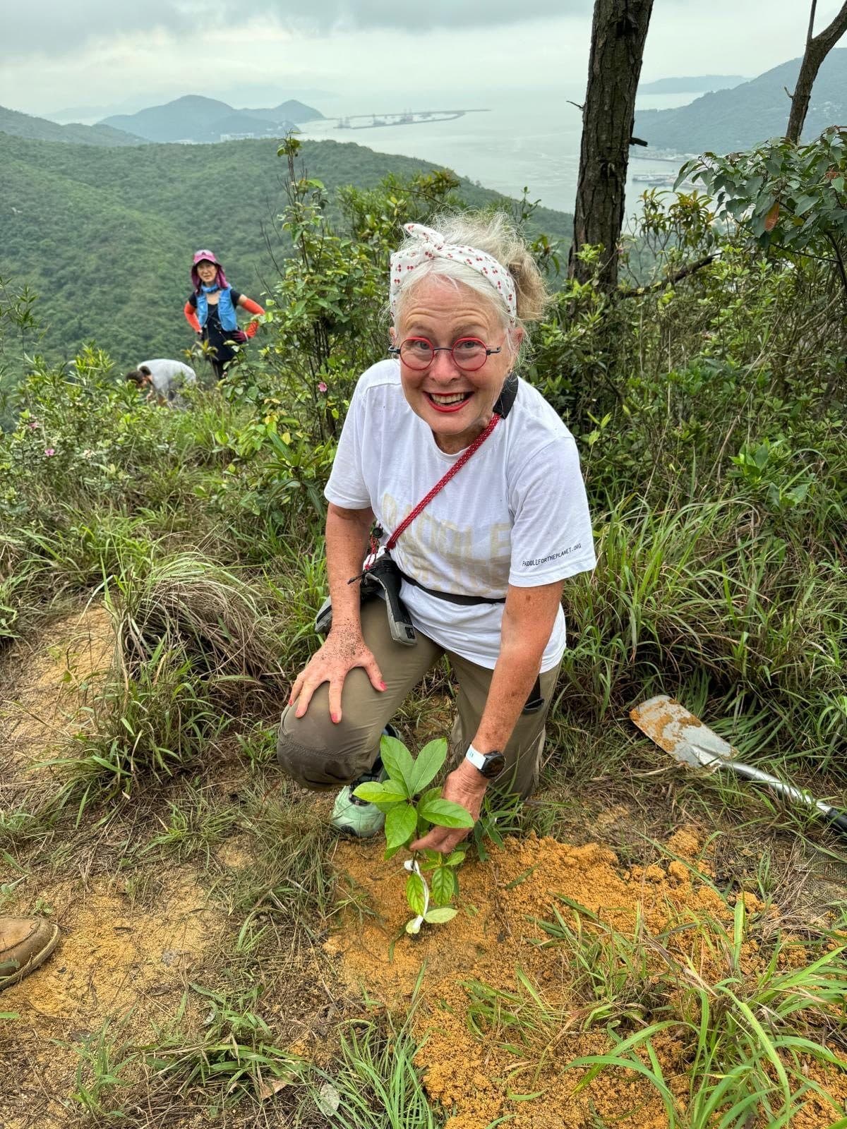 A volunteer kneeling to plant a sapling above the sea on Lantau
