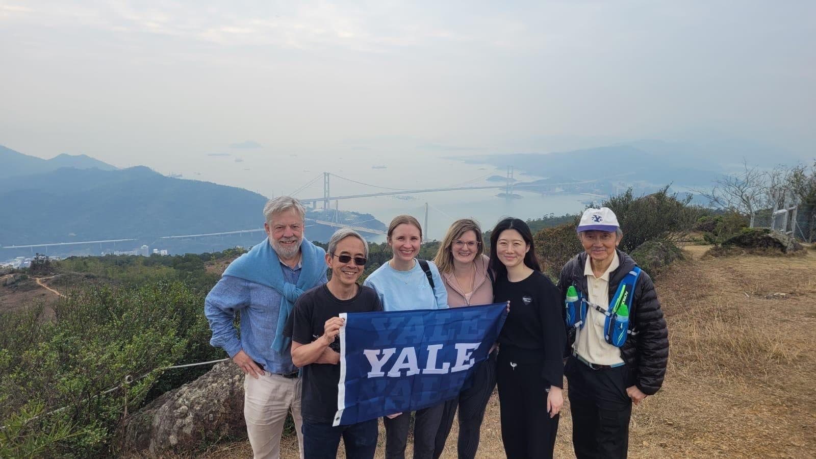 Hikers with a Yale banner above the sea on the Yuen Tsuen Ancient Trail